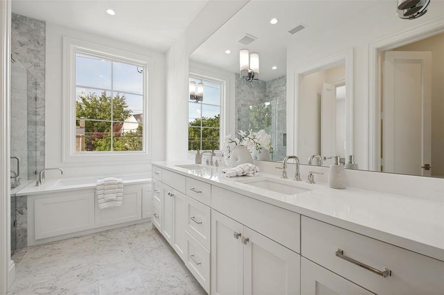 Luxurious primary ensuite featuring designer surfaces, high-end hardware, dual vanities, and a separate soaking tub and walk-in shower. Luxurious primary ensuite featuring designer surfaces, high-end hardware, dual vanities, and a separate soaking tub and walk-in shower.