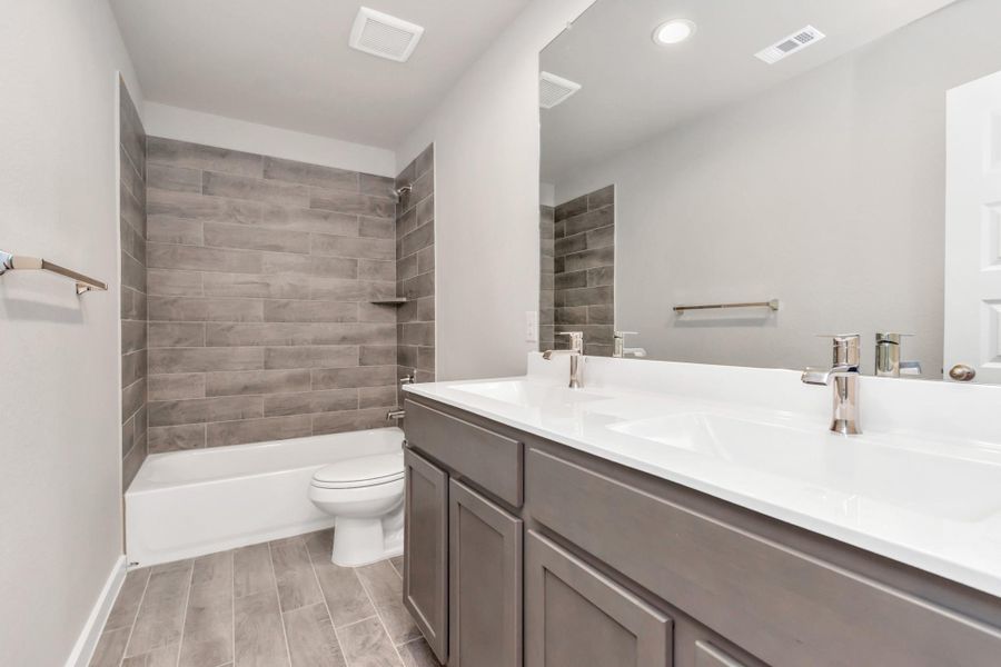 Indulge in refined charm in the secondary bathroom, where the tile flooring harmonizes with a bath/shower combo surrounded by tasteful tile. Dark wood cabinets, double sinks coupled with a gorgeous countertop, elevate the space, cultivating a truly welcoming atmosphere. Sample photo of completed plan. As-built color and selections may vary. Indulge in refined charm in the secondary bathroom, where the tile flooring harmonizes with a bath/shower combo surrounded by tasteful tile. Dark wood cabinets, double sinks coupled with a gorgeous countertop, elevate the space, cultivating a truly welcoming atmosphere. Sample photo of completed plan. As-built color and selections may vary.