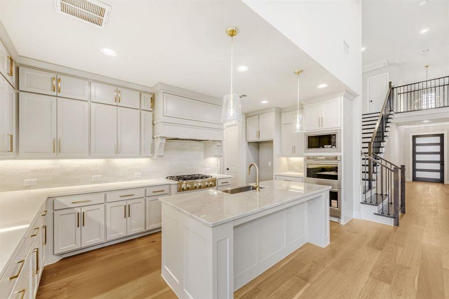 Kitchen featuring light wood-type flooring, a kitchen island with sink, stainless steel appliances, light stone countertops, and white cabinets