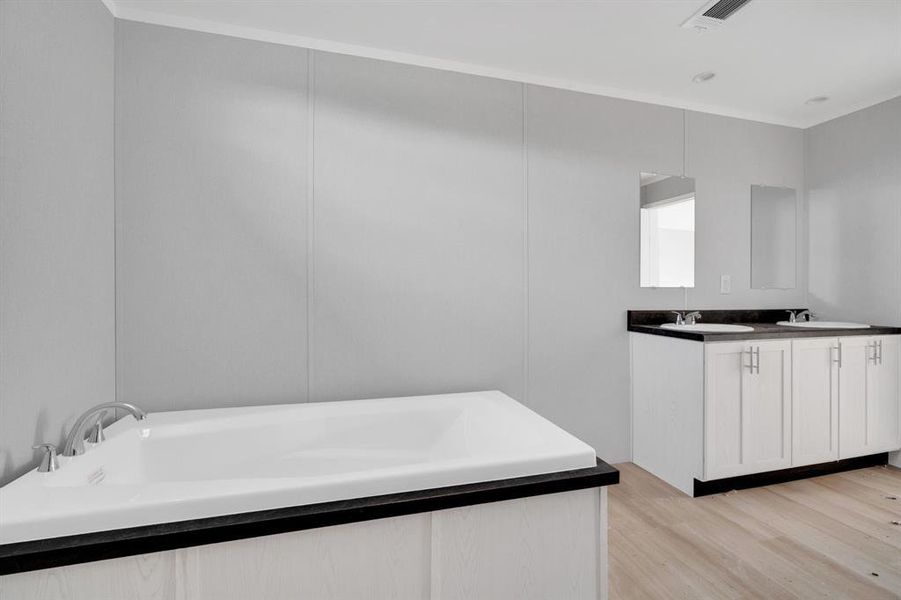 Bathroom featuring double vanity, a garden tub, light wood-style flooring, and a decorative wall