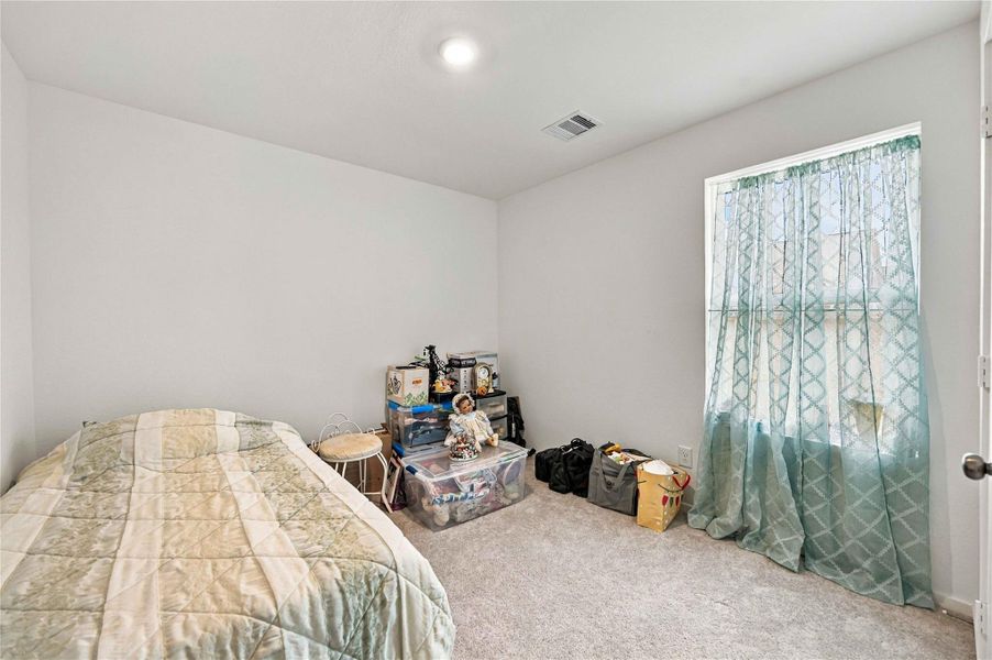 Bright and cozy bedroom featuring soft carpeting, a large window with elegant curtains, and ample space for personalization.