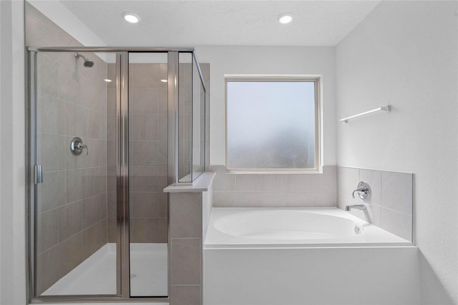 This additional view of the primary bath highlights a soaking tub and separate walk-in shower with tile surround, and a large window that offers both natural light and privacy.