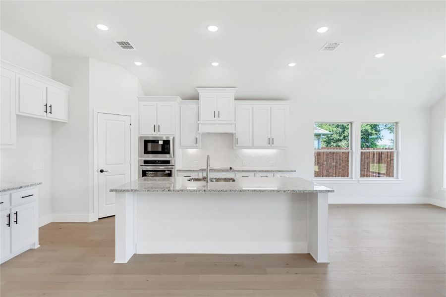 White kitchen with large island, granite countertops, stainless steel appliances, and light hardwood floors