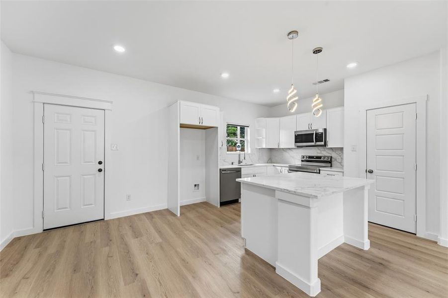 Open-concept kitchen and living area featuring wood-finish flooring, white cabinetry, a kitchen island with a stone countertop, and recessed lighting