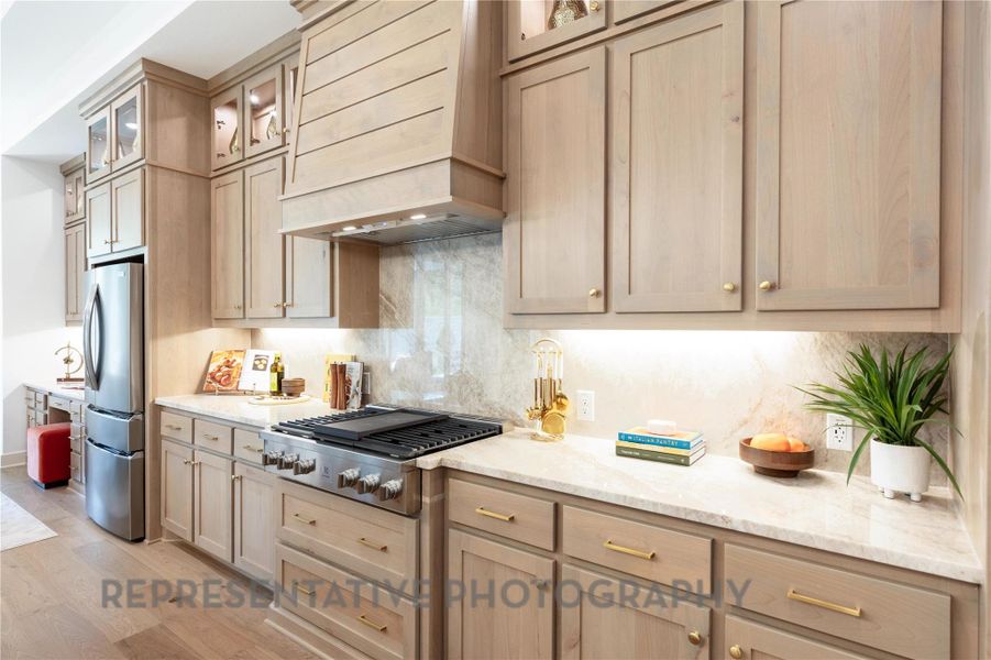 Kitchen with custom range hood, gas stovetop, light wood-style floors, light stone counters, and freestanding refrigerator Kitchen with custom range hood, gas stovetop, light wood-style floors, light stone counters, and freestanding refrigerator