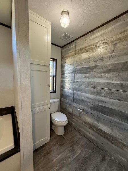 Bathroom with dark wood finished floors, a textured ceiling, wood walls, crown molding, and vanity