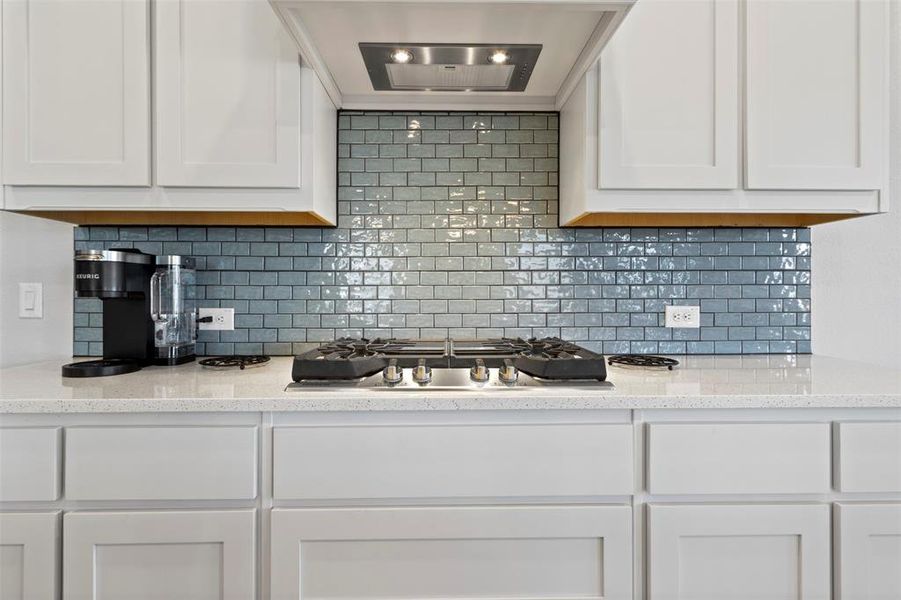 Kitchen with white cabinets, decorative backsplash, stainless steel gas cooktop, and light stone countertops