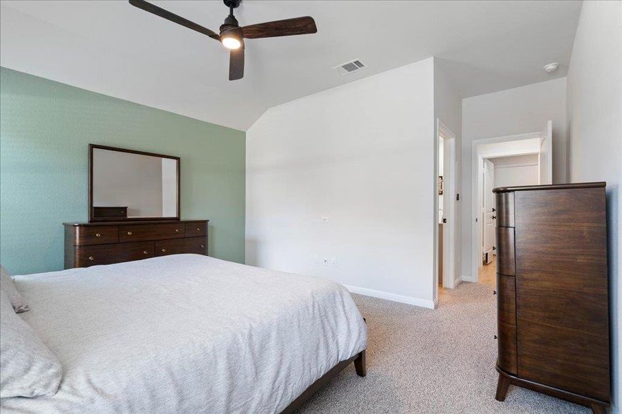 Carpeted bedroom featuring ceiling fan, baseboards, vaulted ceiling, and visible vents