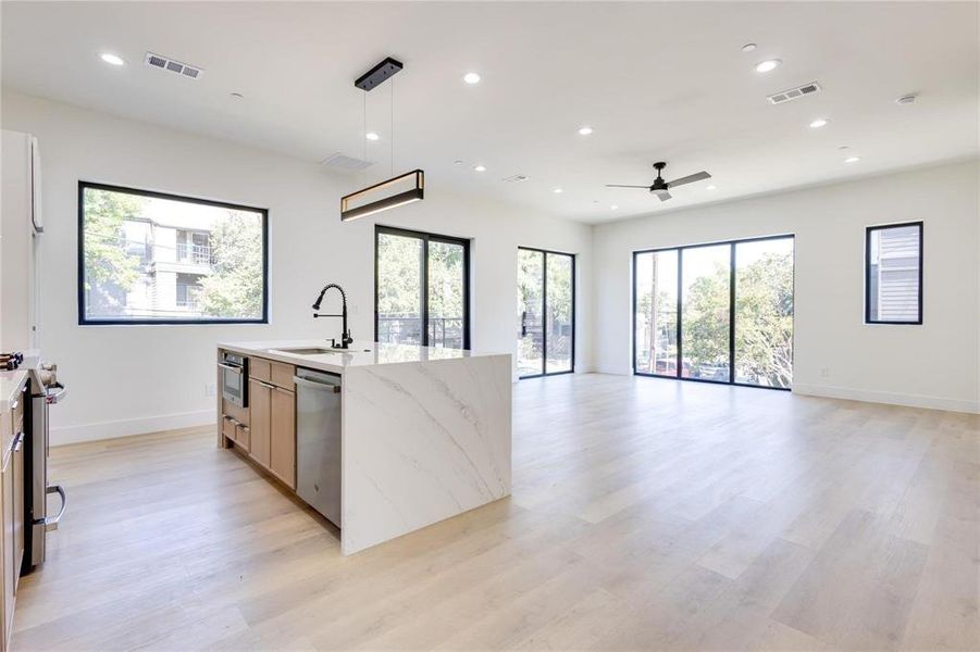 Kitchen with sink, hanging light fixtures, light stone counters, stainless steel appliances, and light wood-type flooring