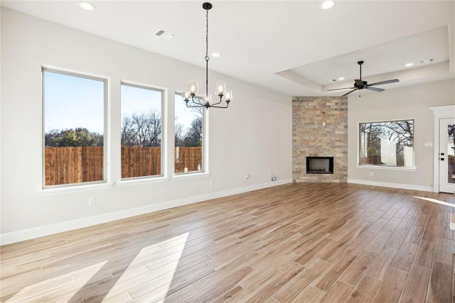 Unfurnished living room featuring ceiling fan with notable chandelier, a fireplace, a wealth of natural light, and a tray ceiling