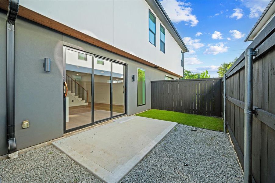Backyard features a concrete patio extending from the rear elevation. Sliding glass doors provide direct access to the interior living area. Turf yard and decorative gravel border complete the outdoor space. Wood privacy fencing surrounds the yard.