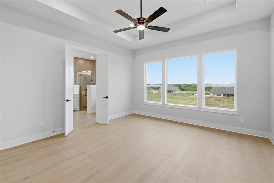 This room features light-colored flooring, a ceiling fan, and a tray ceiling