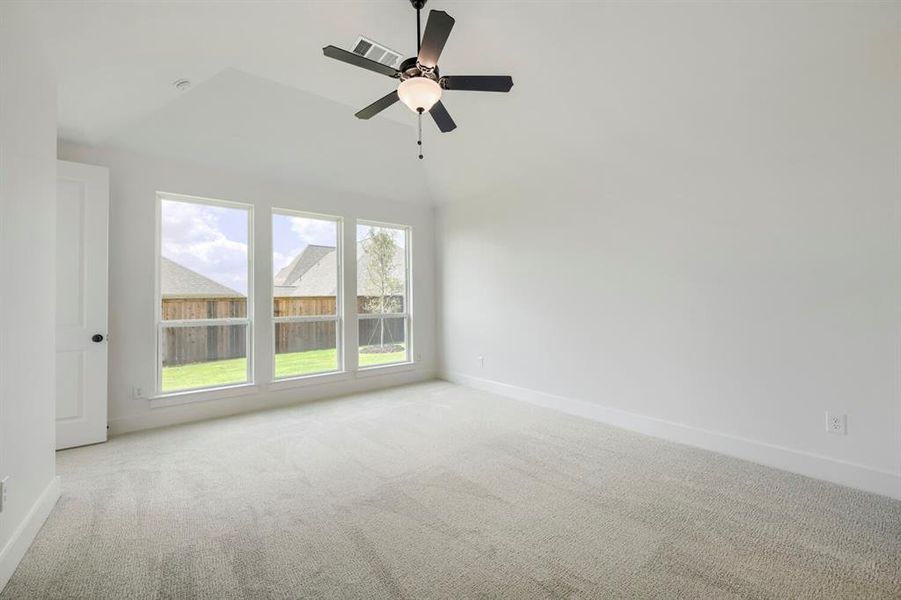 Spacious room featuring vaulted ceilings, a ceiling fan with integrated lighting, and three tall windows providing natural illumination Spacious room featuring vaulted ceilings, a ceiling fan with integrated lighting, and three tall windows providing natural illumination