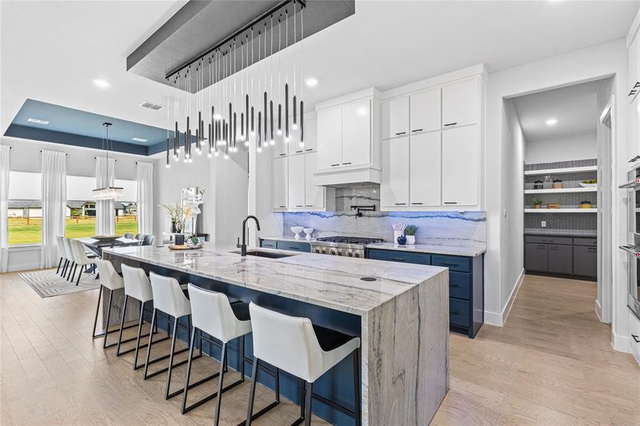 Kitchen with light stone countertops, white cabinetry, a large island, light wood finished floors, and recessed lighting