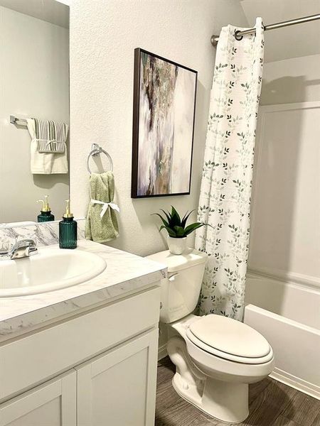 Full bathroom featuring a textured wall, toilet, shower / bath combination with curtain, wood finished floors, and vanity Full bathroom featuring a textured wall, toilet, shower / bath combination with curtain, wood finished floors, and vanity