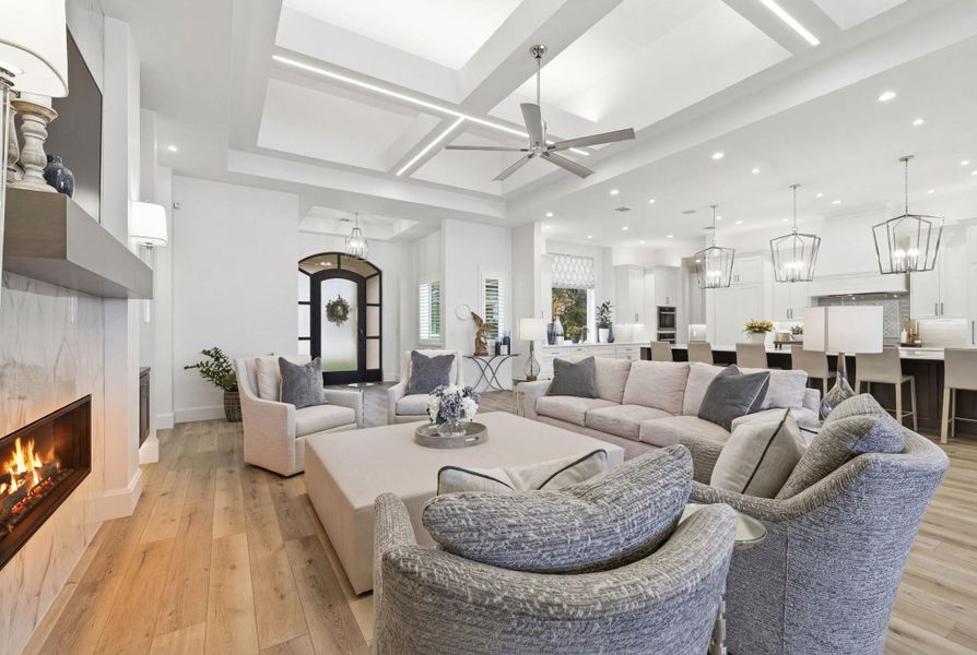 Living room featuring coffered ceiling, a high end fireplace, a chandelier, a ceiling fan, and light wood-style floors
