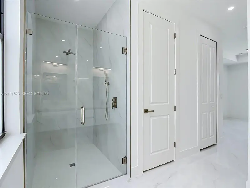 Walk-in shower featuring a frameless glass enclosure, floor-to-ceiling large-format tile surround, rainfall showerhead, handheld sprayer, and polished metallic fixtures