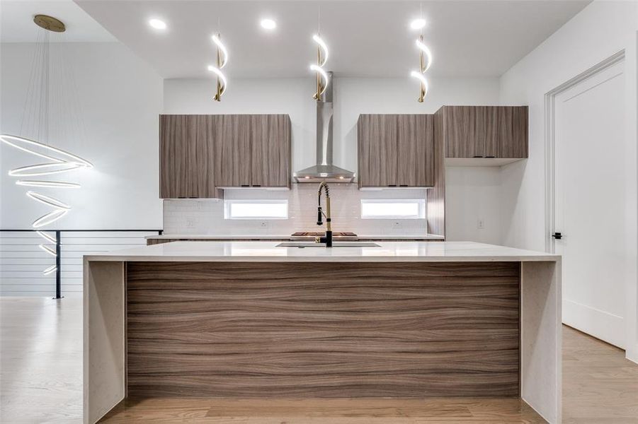 Kitchen with modern cabinets, light countertops, an island with sink, and wall chimney range hood
