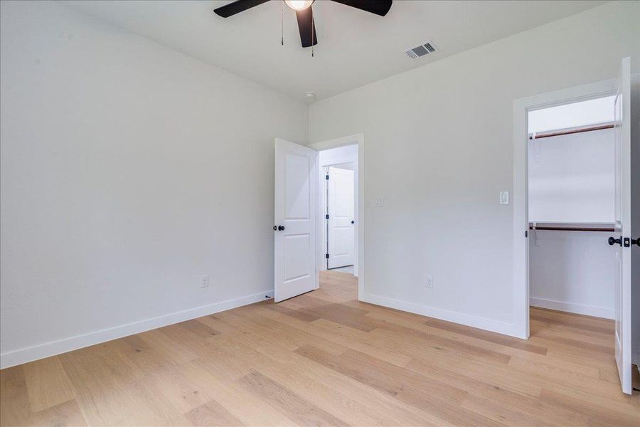 Additional view of the secondary bedroom, a quiet retreat with blonde wood flooring, illuminated by recessed lighting and a sleek ceiling fan.