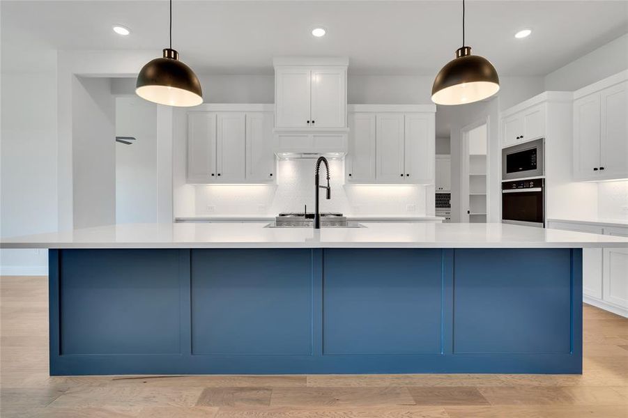 Kitchen featuring backsplash, appliances with stainless steel finishes, light wood-type flooring, and a large island with sink