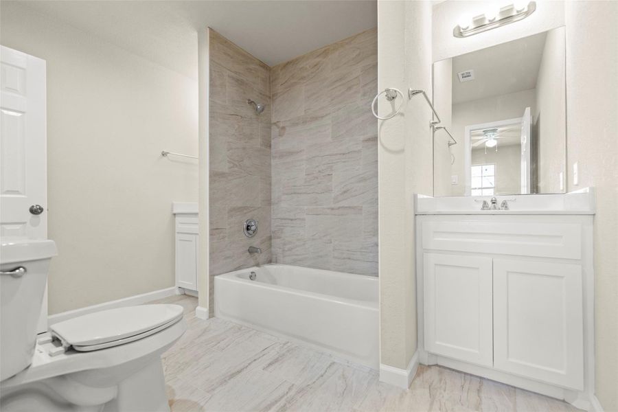 This bathroom features a clean, modern design with a white vanity, a large mirror, and a bathtub with a tiled surround. The neutral color palette offers a bright and spacious feel.