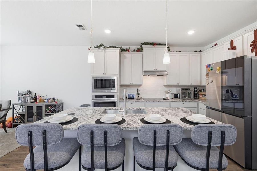 Kitchen featuring appliances with stainless steel finishes, white cabinets, hanging light fixtures, light stone counters, and a kitchen breakfast bar