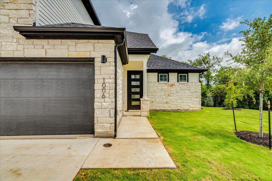 A striking modern facade with contrasting stone and siding, complemented by a pristine lawn.