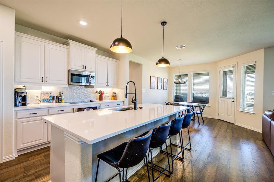 Kitchen featuring a breakfast bar, white cabinets, an island with sink, tasteful backsplash, and dark wood-type flooring