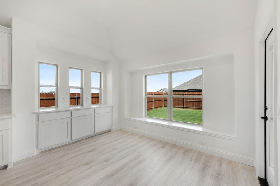 Empty dining area with white built-in cabinets, light wood floors, and large windows overlooking a fenced backyard