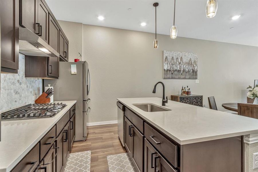 Kitchen with decorative light fixtures, tasteful backsplash, wall chimney exhaust hood, light wood-type flooring, and sink