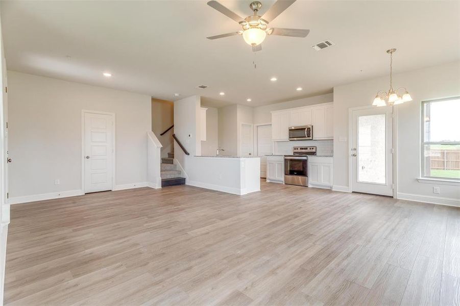 Unfurnished living room with a ceiling fan, light wood-style floors, recessed lighting, a chandelier, and stairs