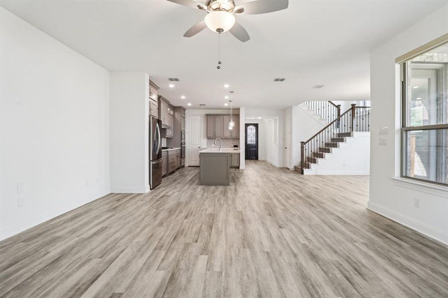 Unfurnished living room with a ceiling fan, stairway, light wood finished floors, recessed lighting, and healthy amount of natural light Unfurnished living room with a ceiling fan, stairway, light wood finished floors, recessed lighting, and healthy amount of natural light