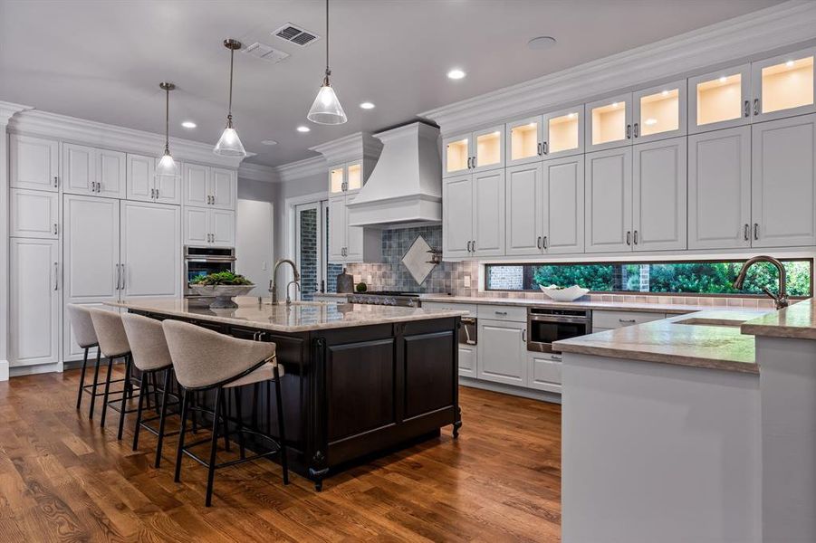 Kitchen featuring decorative light fixtures, light stone countertops, ornamental molding, an island with sink, and a breakfast bar area Kitchen featuring decorative light fixtures, light stone countertops, ornamental molding, an island with sink, and a breakfast bar area