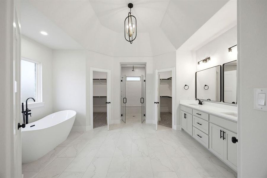 Spacious bathroom featuring a freestanding soaking tub, dual vanities with white cabinetry, a glass-enclosed shower, and two walk-in closets