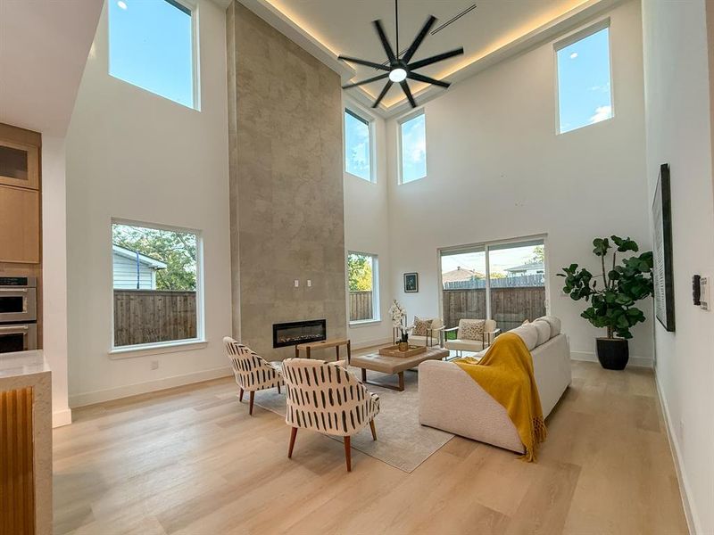Living room with a tile fireplace, light wood-style floors, a towering ceiling, healthy amount of natural light, and ceiling fan