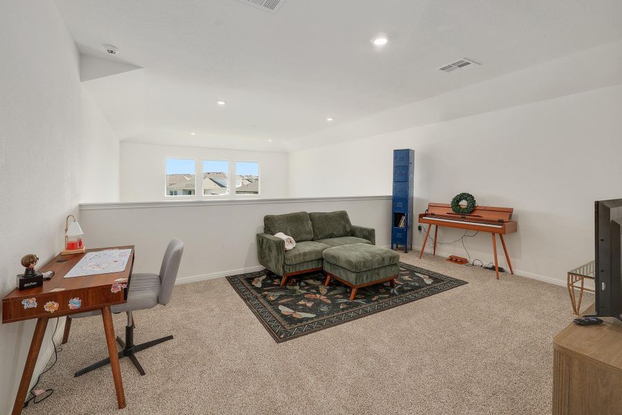 Carpeted loft space featuring recessed lighting, a white half-wall, and three distant windows Carpeted loft space featuring recessed lighting, a white half-wall, and three distant windows
