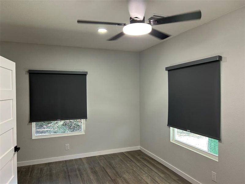 Unfurnished room with dark wood finished floors, a ceiling fan, and plenty of natural light Unfurnished room with dark wood finished floors, a ceiling fan, and plenty of natural light
