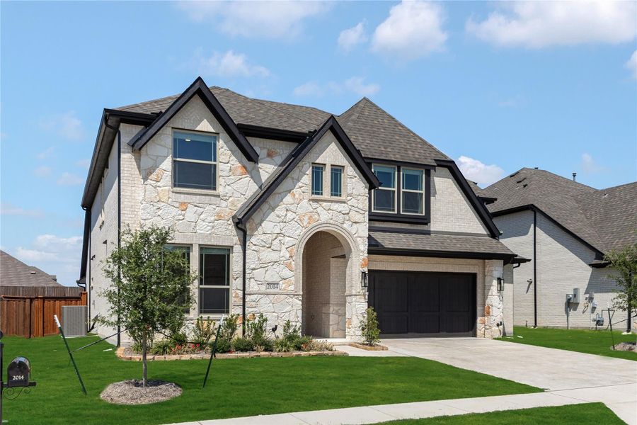 Two-story home with stone and brick exterior, arched entry, two-car garage, and manicured front lawn