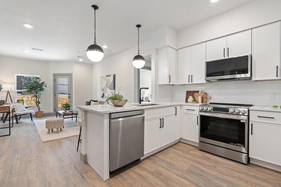 Kitchen with stainless steel appliances, white cabinetry, open floor plan, and pendant lighting