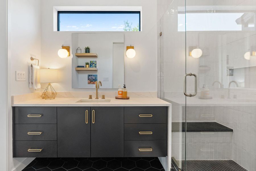 Bathroom featuring a dark wood-finish floating vanity with a light-toned countertop, a glass-enclosed shower with a built-in bench, hexagonal black floor tiling, and a transom window