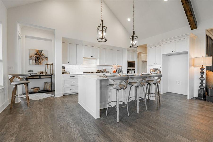 Kitchen with decorative light fixtures, a kitchen island with sink, high vaulted ceiling, white cabinetry, and dark hardwood / wood-style flooring