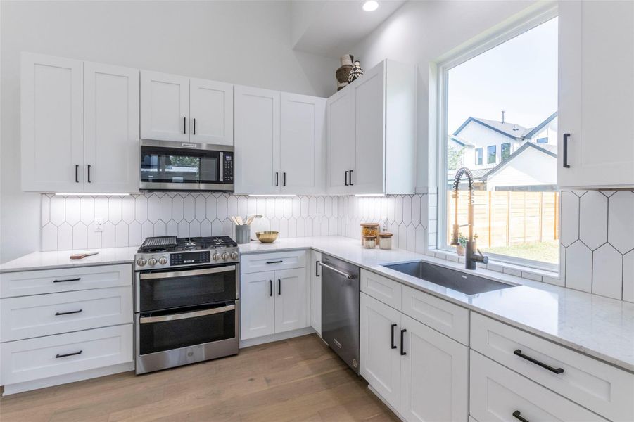 Kitchen with stainless steel appliances, backsplash, light stone counters, and white cabinets