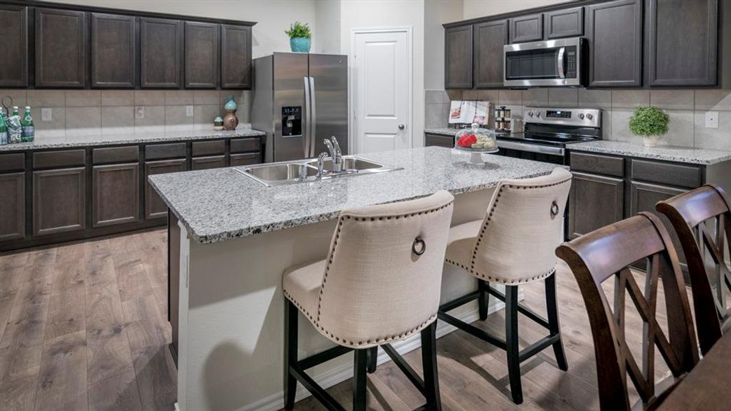 Kitchen with stainless steel appliances, dark wood-style flooring, a center island with sink, a kitchen bar, and light stone countertops
