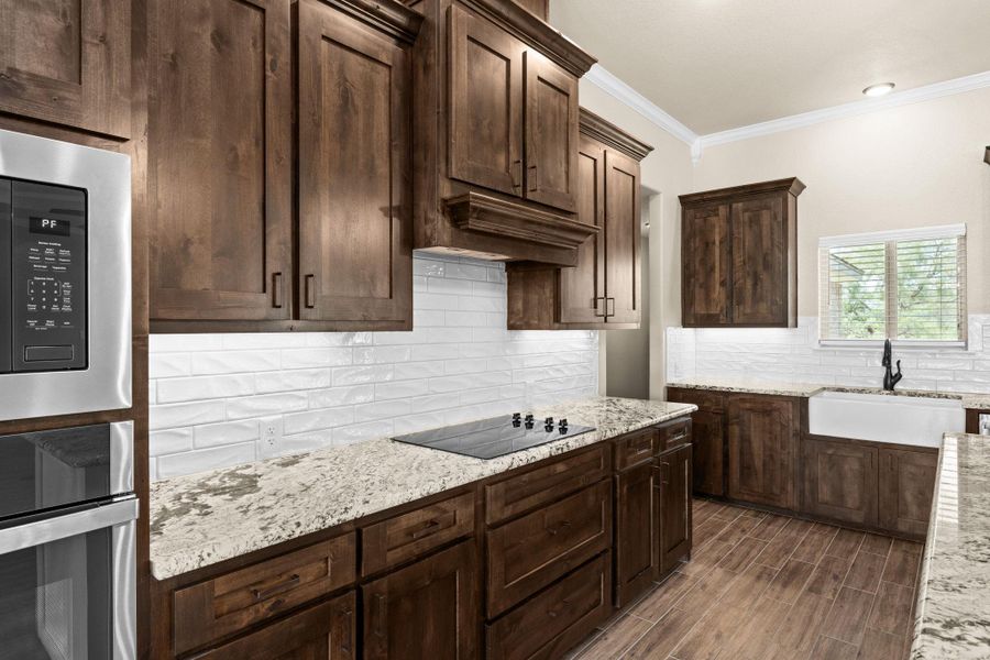 Kitchen featuring backsplash, crown molding, appliances with stainless steel finishes, dark brown cabinetry, and light granite counters Kitchen featuring backsplash, crown molding, appliances with stainless steel finishes, dark brown cabinetry, and light granite counters
