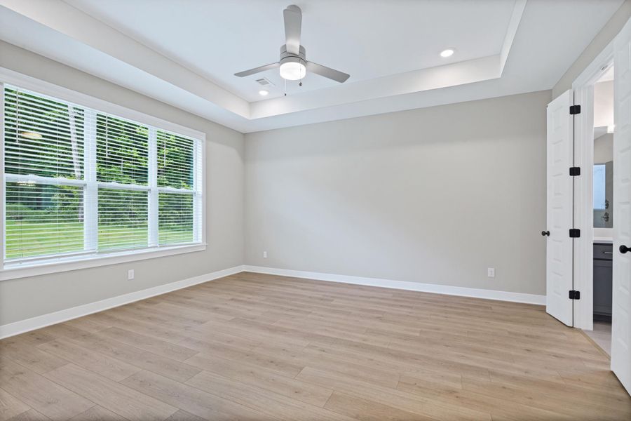 Spacious room featuring wood-finish flooring, a tray ceiling with recessed lighting, and a ceiling fan Spacious room featuring wood-finish flooring, a tray ceiling with recessed lighting, and a ceiling fan