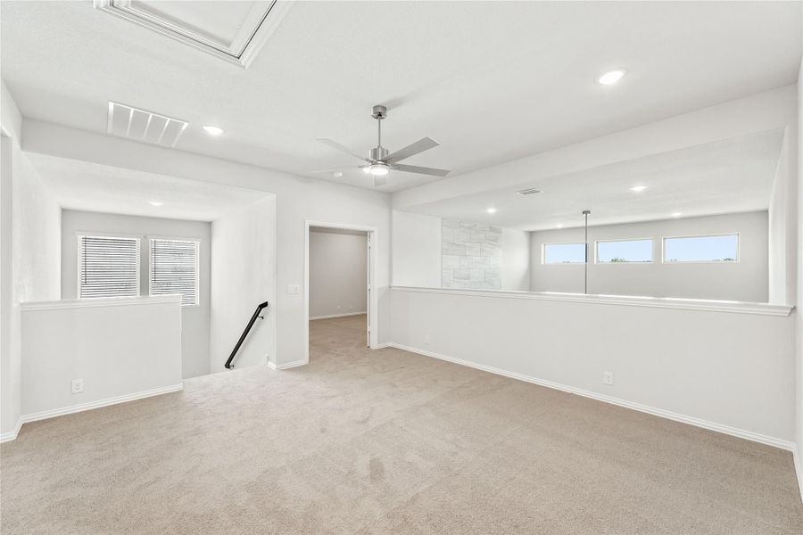 Spacious empty room with beige carpet, ceiling fan, recessed lighting, and open staircase railing Spacious empty room with beige carpet, ceiling fan, recessed lighting, and open staircase railing