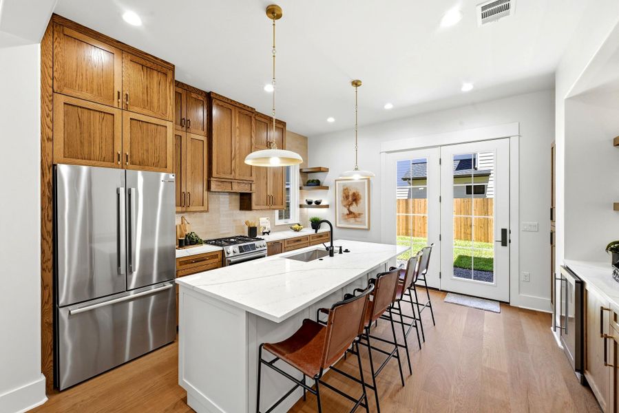 An inviting kitchen features a spacious island with a sink and seating, complemented by warm wood cabinetry and a view of the backyard through glass-paned doors. An inviting kitchen features a spacious island with a sink and seating, complemented by warm wood cabinetry and a view of the backyard through glass-paned doors.