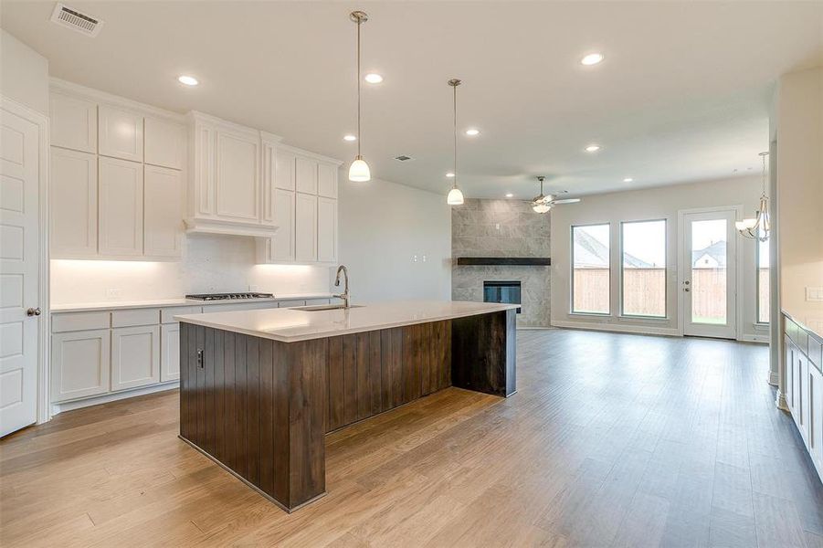 Kitchen featuring a fireplace, white cabinets, stainless steel gas stovetop, light hardwood / wood-style floors, and a kitchen island with sink