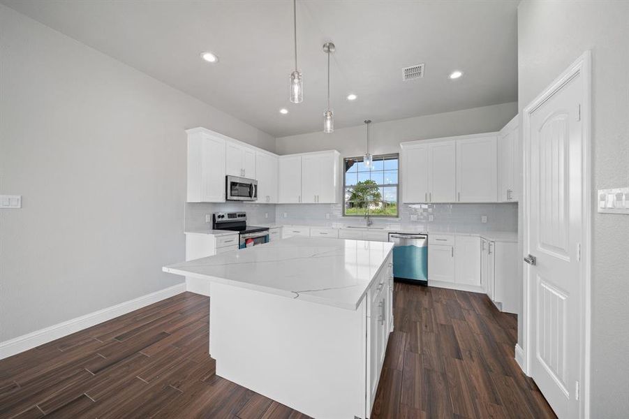 Kitchen with tasteful backsplash, stainless steel appliances, white cabinets, a center island, and dark wood-type flooring