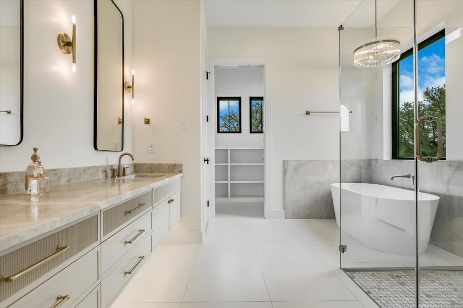Modern bathroom featuring a freestanding soaking tub, a frameless glass shower enclosure, a dual vanity with a light-colored countertop, and a walk-in closet with built-in shelving